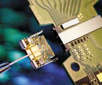 aПередающий модуль Silicon Photonics (слева) испускает лазерный луч, формируемый под управлением кремниевой микросхемы в центре зеленой платы; этот луч затем проходит через оптоволокно в принимающий модуль (справа), где вторая кремниевая микросхема распознает передаваемые данные и вновь превращает их в электрические сигналы